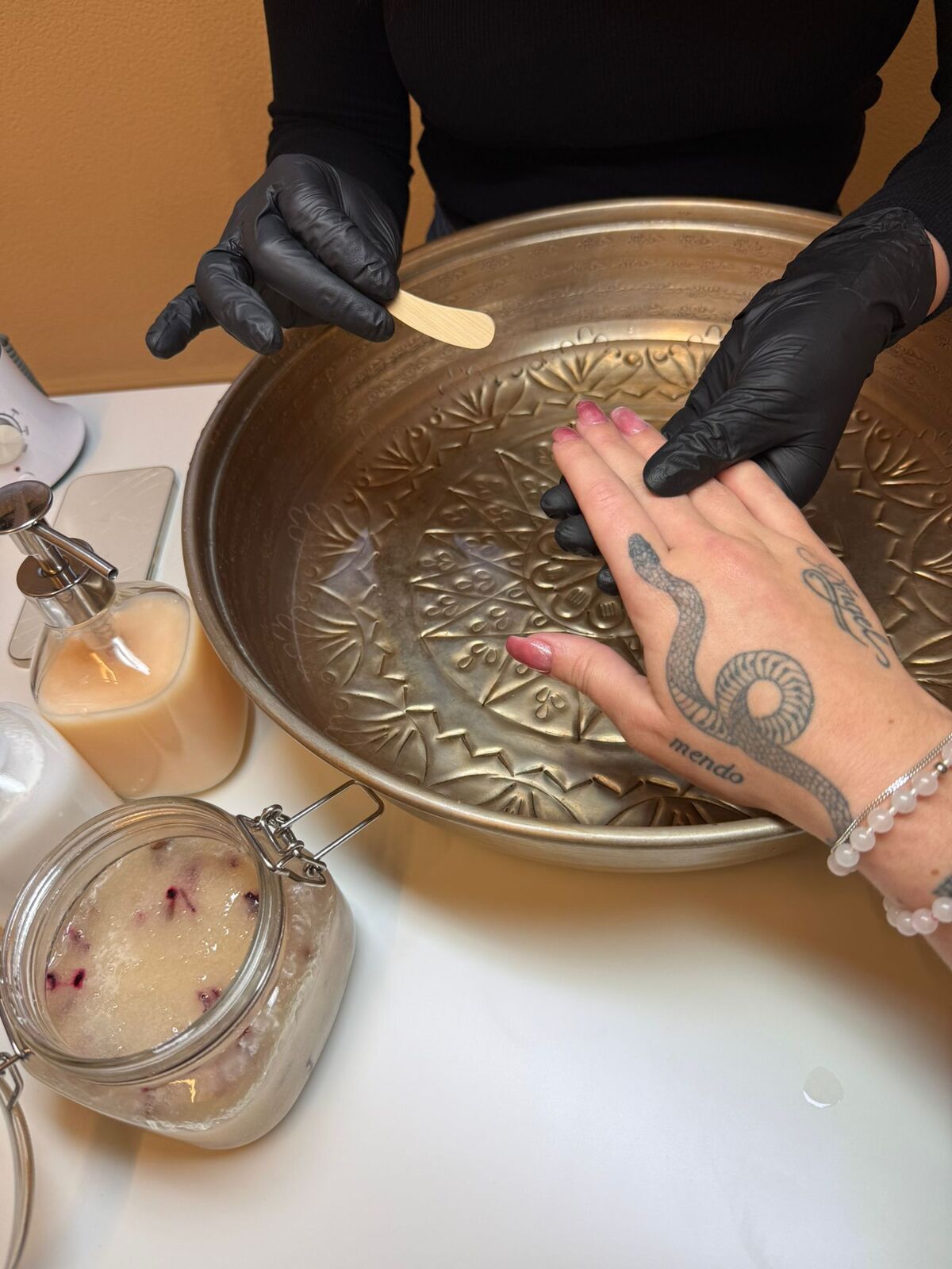 Handpflege im Salon: Hände werden über einer verzierten Messingschale mit Peeling und Pflegeprodukten verwöhnt